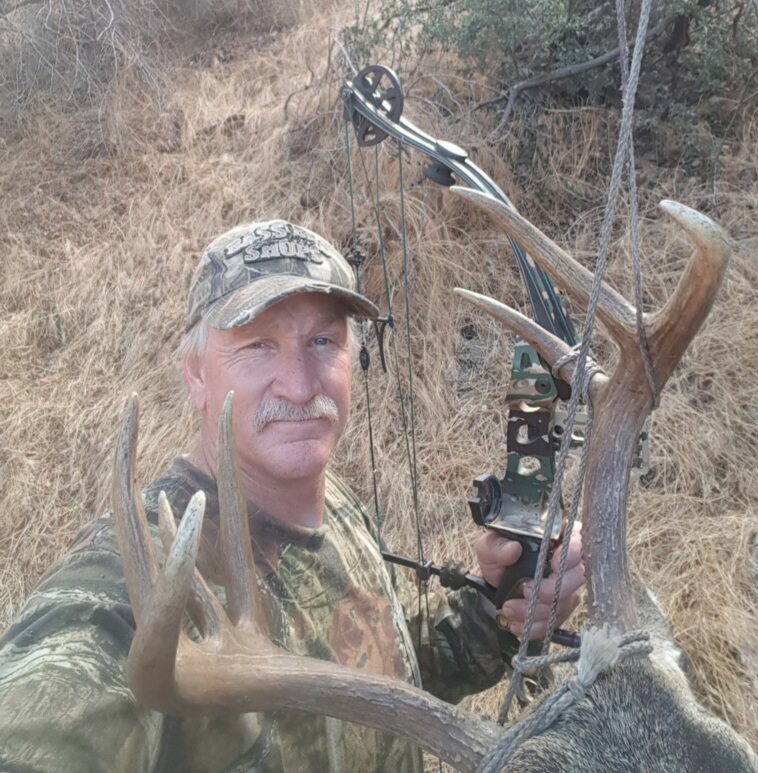 closeup of owner Clay L. Fairres in camo hunting clothes with deer and hunting bow